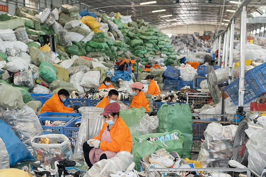 several sorters working through bales of used branded shoes